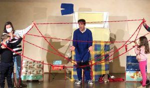 Matteo Razzini ha davanti a sè un intreccio di fili rossi retti alle estremità da 2 adulti e 2 bambini del pubblico